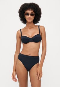 Black bikini set featuring a ribbed texture, a structured underwire top with adjustable straps, and high-waisted bottoms for coverage.