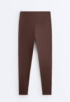 Leggings marroni a vita alta con finitura liscia e dettaglio con cucitura a forma di V sulla fascia in vita, presentati distesi su uno sfondo bianco.