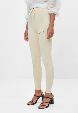 Beige leggings med justerbar talje, sidelommer og sort skrift på låret. Fremstillet af blødt, strækbart stof.