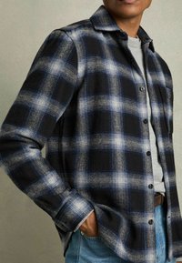 Schwarz-blau kariertes Hemd aus wolkenähnlichem Material, mit einer Knopfleiste, Kragen und langen Ärmeln in lockerer Passform.