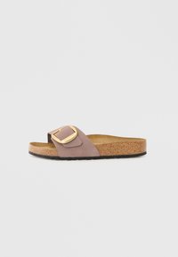 Brun korkfotbäddssandaler med mjukt mauve ovansida, med en stor guldspänneaccent. Platt sula, avslappnad design.