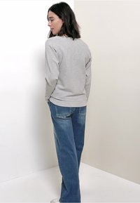 Graues, gestreiftes Langarmoberteil mit rundem Halsausschnitt, kombiniert mit hellblauen, weit geschnittenen Jeans. Von hinten vor einem schlichten Hintergrund präsentiert.