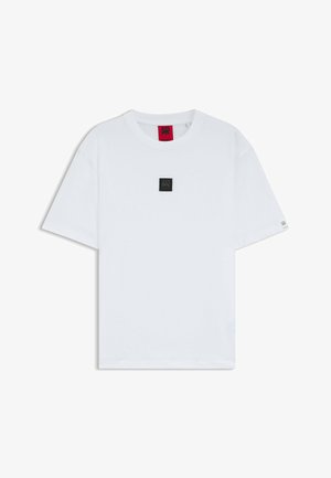 Vit bomullströja med rundad halsringning, kortärmar och en liten svart fyrkantig logotyp på bröstet. Lappen synlig inuti kragen.