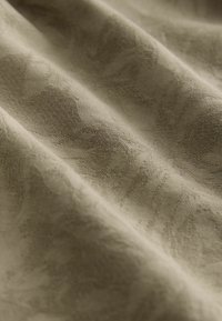 Texturiertes Gewebe in einem gedämpften Olivgrün, mit einem subtilen Blumenmuster, sanftem Glanz und fließendem Erscheinungsbild, das die Details des Gewebes hervorhebt.