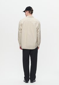 Beige overhemd met lange mouwen en een button-down kraag, gedragen met zwarte broeken. Het shirt heeft een gestructureerde stof en een rechte snit.