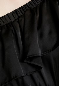 Svart, silkesliknande tyg med volangdetaljer vid halslinningen. Har ett elastiskt midjeband och en mjuk struktur. Inga synliga mönster eller detaljer.