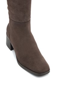 Barna velúr, középig érő csizma négyzetes orral és alacsony, rakott sarokkal, elölnézetből, fehér háttér előtt bemutatva.