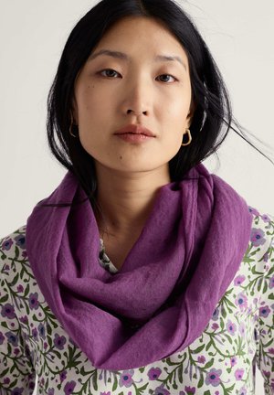 Lilla tørklæde lavet af blødt materiale, løst draperet omkring halsen. Personen har mørkt hår og bærer en skjorte med blomsterprint.