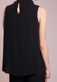 Svart utanärmad topp i lätt tyg, med en detalj i form av nyckelhål bak, avslappnad passform och rundad nederkant.