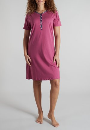 Frau trägt ein knielanges, kurzärmeliges rosa Nachthemd mit marineblauem Blumenbesatz am runden Ausschnitt und an der Vorderleiste.