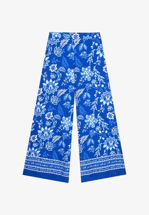 Pantalon à jambes larges avec motifs floraux bleus et blancs et bandes décoratives le long de l'ourlet sur un fond blanc uni.