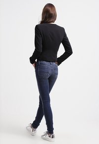 Svart figursydd jacka med lång ärm, i kombination med mörkblå skinny jeans och metalliska silver sneakers. Slätt tyg och strömlinjeformat mönster.