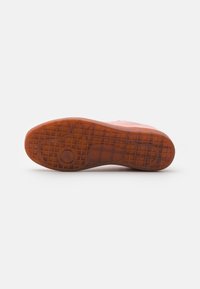 Suela de un zapato de goma con una superficie texturizada, que presenta un patrón de cuadrícula y un detalle circular elevado, principalmente en tonos marrón-naranja.