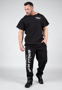 Zwart sportoutfit met een losse, gestructureerde T-shirt met korte mouwen en tapered broeken met een witte logo-print aan de zijkant.
