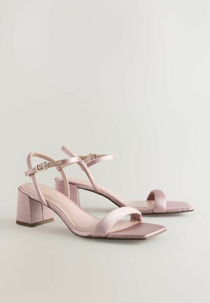 Sandales à talons hauts en satin rose, présentant un bout carré, de fines lanières de cheville et des talons blocs pour plus de stabilité. Agrémentées de détails minimalistes.