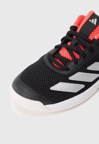 Sort atletiksko med hvid sål, rød mesh-tunge, sorte snørebånd og hvide diagonale striber på siden.