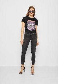 Fekete pamut póló, színes Metallica grafikával, fekete skinny farmerral és fekete magassarkú szandállal párosítva.