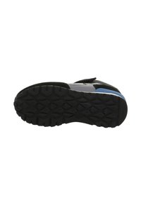 Černá gumová podrážka s hlubokými drážkami na šedé a modré tenisce zobrazené zespodu.