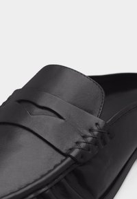 Μαύρο δερμάτινο μοκασίνι με κλασική λωρίδα και χειροποίητες ραφές κατά μήκος της περιοχής των δακτύλων.