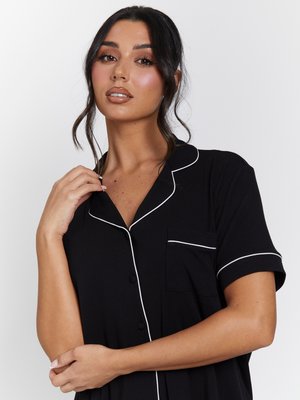 Zwarte geribbelde pyjamashirt met korte mouwen, witte bies, een borstzak en een knopenrij. Glad materiaal en comfortabele pasvorm.