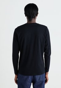 Camiseta negra de manga larga hecha de algodón, con cuello redondo, corte relajado y textura suave, combinada con pantalones de mezclilla azules.