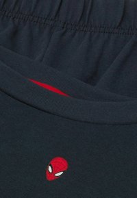 Dunkelblaues T-Shirt mit rundem Halsausschnitt und elastischem Bund. Besitzt ein kleines, rotes, gesticktes Spiderman-Logo auf der Brust.