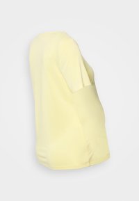Top amarelo de manga curta com decote redondo. Feito de um tecido suave, apresenta um corte solto que afunila na cintura. Exibido em vista lateral.