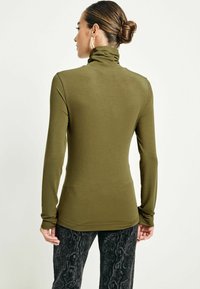 Olivgrön långärmad polotröja med en figurnära design, mjuk textur och ett stretchigt material, parat med svarta mönstrade byxor.