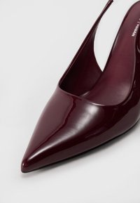Talons slingback en cuir verni bordeaux avec un bout pointu, une finition lisse et une découpe sur le côté, présentant un design minimaliste.