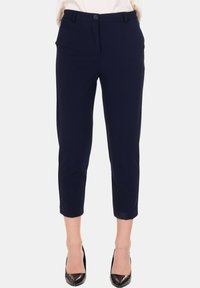 Pantaloni blu navy su misura alla caviglia con bottone frontale e passanti per cintura, indossati con décolleté nere a punta.