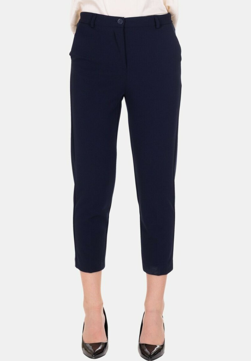 Pantaloni blu navy su misura alla caviglia con bottone frontale e passanti per cintura, indossati con décolleté nere a punta.