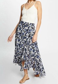Falda maxi floral con un patrón abstracto en azul, blanco y negro; con un dobladillo ondulado y fluido; combinada con una camiseta de tirantes blanca de canalé y sandalias doradas.