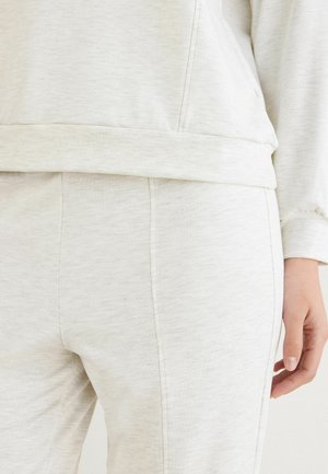 Světlé šedé loungewear set oblečení s texturovanou, měkkou tkaninou. Mikina má volný střih; kalhoty mají slim střih s viditelnými švy.