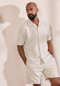 Camicia a maniche corte con colletto e pantaloncini abbinati, entrambi in tessuto leggero, con motivo a righe verticali in tonalità di verde e beige.