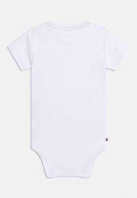 Απλό λευκό βρεφικό φορμάκι με κοντά μανίκια, στρογγυλή λαιμόκοψη, όψη από πίσω και μικρή ετικέτα υφάσματος στη ραφή της πλαϊνής πλευράς.