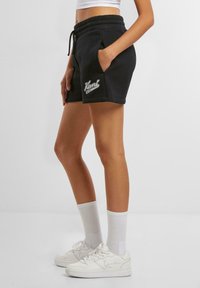 Schwarze Baumwollshorts mit elastischem Bund und Kordelzug, ausgestattet mit Seitentaschen und weißem Logodetail am linken Bein.