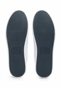 Soli di sneaker bianchi con grip in gomma grigia scura testurizzata. Presenta un'etichetta logo rettangolare nera con la scritta "TOMMY HILFIGER."
