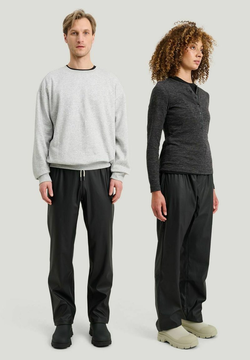 Mand i lysegrå sweatshirt og sorte bukser står ved siden af en kvinde i mørkegrå henley og sorte bukser, begge iført gummisålede sko.