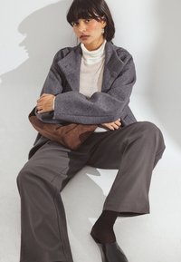 Pelēks paliels vilnas mētelis ar izgriezumu apkakli, krēmkrāsas augstā apkakle, brūna zamšādas somiņa, tumši bikses un melnas bezsvaru kurpes.