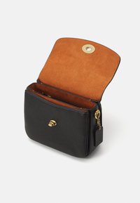 Svart läderväska med en inredning i beige mocka. Har en framfästning med en gyllene knapp och ett blixtlåsrum. Strukturerad rektangulär form.