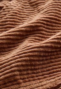 Tessuto di velluto a coste marrone con texture rigata, caratterizzato da righe verticali regolarmente distanziate e un aspetto morbido e vellutato.