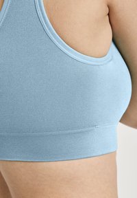 Jasnoniebieski stanik sportowy z teksturowanej tkaniny, z okrągłym dekoltem i szerokim, elastycznym pasem na dole.
