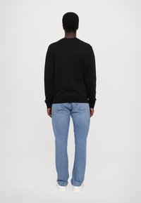 Felpa nera, colletto rotondo, tessuto morbido, abbinata a jeans slim-fit azzurri chiari, sneakers bianche; design minimalista, senza loghi visibili.