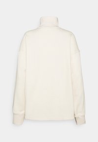 Krämfärgad pullover med hög krage. Har en avslappnad passform, långa ärmar och ribbade muddar, tillverkad av mjukt tyg med en slät struktur.