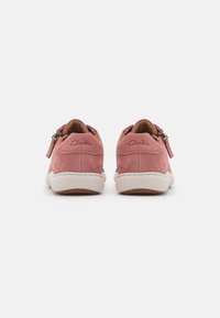 Baskets en daim rose avec semelles blanches, équipées d'une fermeture éclair et d'un logo "Clarks" en relief au niveau du talon. Design arrondi avec une texture douce.