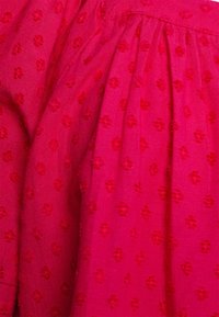 Tessuto rosa brillante con motivo floreale texturizzato, caratterizzato da pieghe e una trama liscia e leggera. I dettagli sono in una tonalità di rosa leggermente più scura.