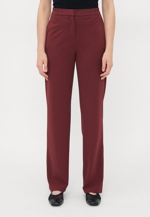 Bordeaux brede broek gemaakt van een gladde, rekbare stof; heeft een elastische tailleband en zijzakken. Gekleed met zwarte platte schoenen.