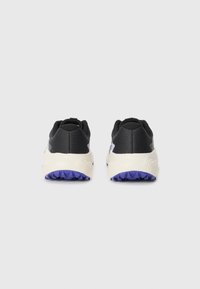 Baskets de sport noires avec une finition texturée, dotées d'une semelle intermédiaire blanche et d'une semelle extérieure en caoutchouc violet, conçues pour l'adhérence et le confort.
