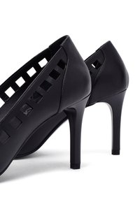 Chaussures à talons hauts noires avec des designs rectangulaires découpés, finitions en cuir lisse, talons effilés et accents carrés près de la base du talon.