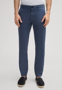 Chino blu navy realizzati in tessuto leggero, caratterizzati da una vestibilità slim, chiusura con bottone e design a vita piatta, abbinati a scarpe nere slip-on.